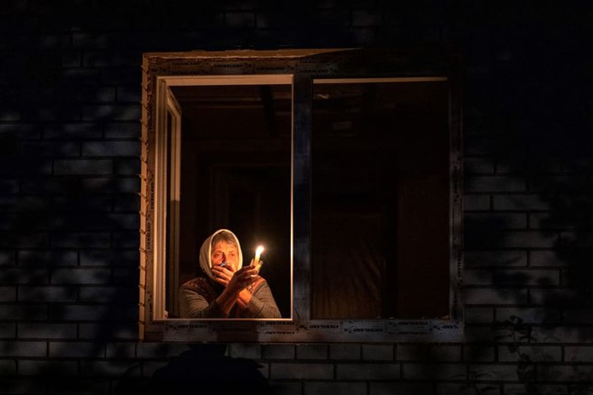 Una mujer alumbra con una vela desde su ventana ante los cortes de electricidad en Ucrania.