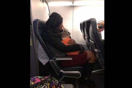 Una mujer ayuda a otra madre a cargar a su hijo en brazo durante un vuelo