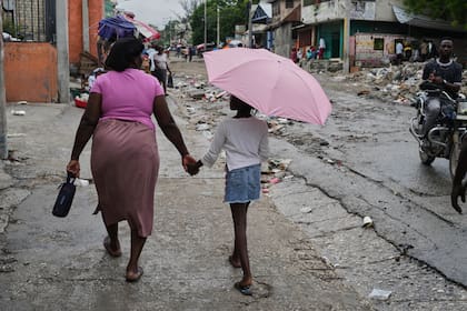 Una mujer camina de la mano con una chica con paraguas bajo una suave lluvia en Puerto Príncipe, Haití, el 23 de octubre de 2025