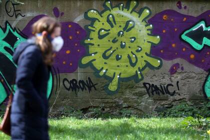 Una mujer camina frente a una pared con un graffiti relacionado con el coronavirus, en Edimburgo, Escocia