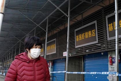 Una mujer camina frente al mercado mayorista de mariscos de Huanan, que fue cerrado y donde las autoridades dicen que se originó el primer brote de la enfermedad respiratoria en Wuhan