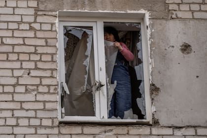 Una mujer coloca un plástico sobre los vidrios rotos de una ventana tras un ataque ruso en la víspera, en la zona residencial de Mikolaiv, Ucrania, el 29 de marzo de 2022. (AP Foto/Petros Giannakouris)