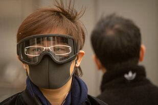 Una mujer con mascarilla y gafas protectoras camina por una calle del distrito central de negocios de Pekín, el 22 de marzo de 2023.