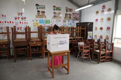 Una mujer con un niño en brazos emite su voto durante la segunda vuelta de las elecciones presidenciales en un colegio electoral del distrito de San Juan de Lurigancho