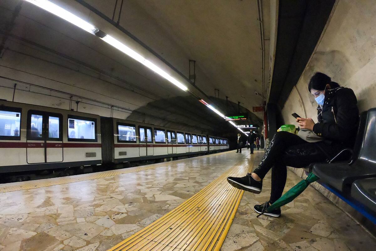 Una mujer con un tapabocas mira su celular en la estación de metro Coliseo de la línea B, en medio de la pandemia del coronavirus, en Roma