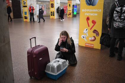 Una mujer con una maleta y un porta gatos cerrado revisa su teléfono en una estación de metro en Kiev.