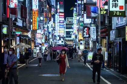 Una mujer con una máscara facial camina con un paraguas por una calle en el distrito Kabukicho de Tokio el 24 de junio de 2020