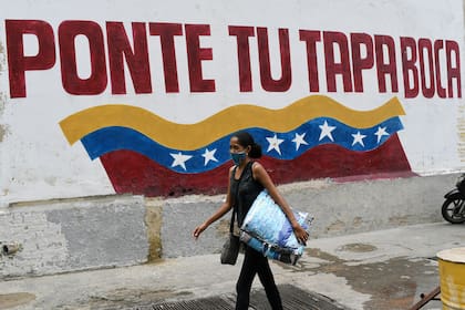 Una mujer con una mascarilla protectora pasa junto a un mural con un mensaje que dice en español: "Ponte la mascarilla" en el barrio Catia de Caracas, Venezuela, el sábado 5 de septiembre de 2020, en medio de la nueva pandemia de coronavirus.