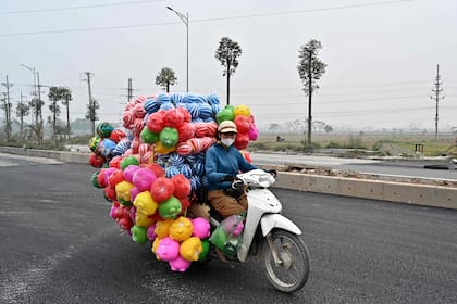 Una mujer conduce una motocicleta que transporta juguetes de plástico en las afueras de Hanoi