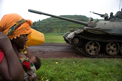 Una mujer congoleña que lleva a su hijo y sus pertenencias pasa junto a un tanque del ejército congoleño cerca de Kibumba, foto de Walter Astrada de una serie que denuncia las violaciones de mujeres en la guerra del Congo