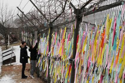 Una mujer cuelga un lazo deseando la reunificación de las dos coreas en una cerca durante una visita al Pabellón de Imjingak, cerca de la frontera con el Norte, para celebrar el Año Nuevo Lunar en Paju, Corea del Sur, el domingo 22 de enero de 2023. (AP Foto/Ahn Young-joon)