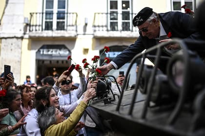 Una mujer de 90 años que entregó claveles a los militares en la revolución pacífica de 1974 le entrega una flor a un exmilitar durante los festejos del 50 aniversario