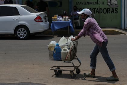 Una mujer empuja un carrito cargado con botellas de agua recolectadas de una canilla en una calle de Maracaibo (Archivo)