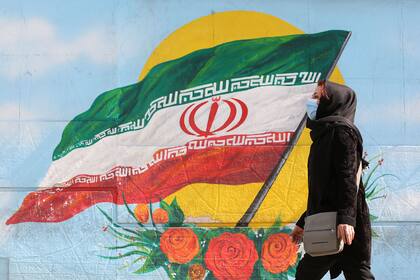 Una mujer pasa frente a un mural con la bandera de Irán, un país afectado al mismo tiempo por la pandemia y las sanciones debidas a su programa nuclear