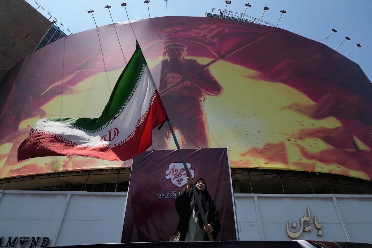 Una mujer ondea una bandera iraní junto a una valla publicitaria que muestra la imagen de un hombre con una camiseta que trae el rostro del difunto líder supremo iraní, el ayatolá Alí Jamenei --quien murió durante un ataque conjunto de Estados Unidos e Israel el 28 de febrero--, con palabras que invocan a los vengadores del imán Hussein, uno de los santos más venerados del islam chií, el sábado 1 de agosto de 2026, en una plaza del centro de Teherán, Irán. (AP Foto/Vahid Salemi)