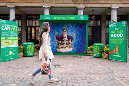 Una mujer pasa frente a la instalación de una corona hecha con latas recicladas, en Covent Garden Market, Londres