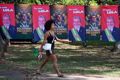 Una mujer pasa junto a banderas y toallas que exhiben las imágenes del presidente de Brasil y candidato presidencial, Luiz Inácio Lula da Silva, y del senador de derecha y también candidato presidencial, Flavio Bolsonaro, en Brasilia