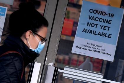 Una mujer pasa junto a un letrero que dice "La vacuna contra el coronavirus aún no está disponible" afuera de una tienda en Arlington, Virginia, el 1 de diciembre de 2020