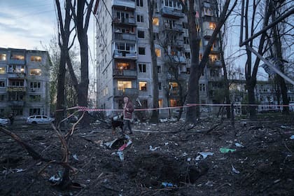 Una mujer pasea con un perro entre los escombros de una casa dañada en un ataque ruso a una zona residencial en Kiev
