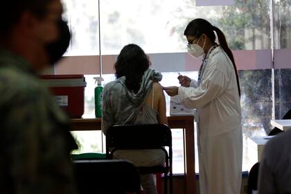 Una mujer recibe su vacuna contra el COVID-19 en Quito, Ecuador, el jueves 23 de diciembre de 2021. El gobierno de Ecuador suspendió el viernes 7 de enero de 2022 las clases en el sistema público y aceleró la vacunación de los docentes ante la aceleración en los contagios en la población infantil. (AP Foto/Carlos Noriega)