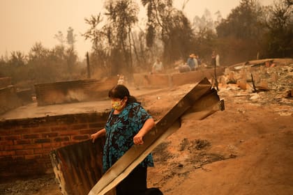 Una mujer remueve escombros en un paisaje devastado por el fuego en Santa Ana, Chile, sábado 4 de febrero de 2023. Al menos 13 personas han muerto en los incendios que han destruido viviendas y miles de hectáreas de bosques en el sur de Chile. (AP Foto/Matias Delacroix)