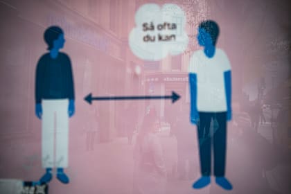 Una mujer se refleja en un anuncio de los servicios de salud de Suecia para instruir a las personas a seguir la regla de los 2 metros para reducir el riesgo de enfermarse de Covid-19 en Estocolmo el 4 de mayo de 2020