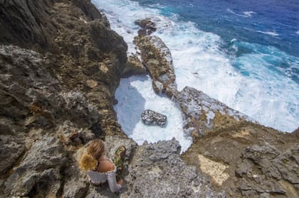 Una mujer sentada sobre una roca con vistas al océano en Niue