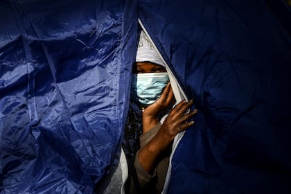 Una mujer somalí se asoma desde su tienda en un campamento improvisado que alberga a más de 50 inmigrantes, incluidos refugiados y solicitantes de asilo, a lo largo del Bassin de la Villette en París el 27 de mayo de 2020