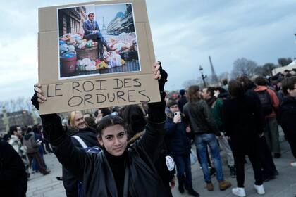 Una mujer sostiene un cartel con una imagen del presidente de Francia, Emmanuel Macron, sentado sobre una pila de basura con la franse "rey de la basura", durante una protesta en París, el 17 de marzo de 2023. (AP Foto/Lewis Joly)