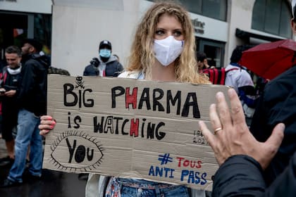 Una mujer sostiene un cartel que dice "Las grandes farmacéuticas lo están mirando" durante una protesta contra las vacunas y los pasaportes de vacunas, en París, Francia, el sábado 7 de agosto de 2021