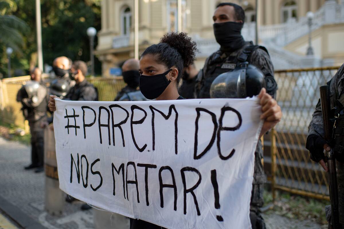 Una mujer sostiene una pancarta que dice "Dejen de matarnos" frente a una línea de policías antidisturbios durante una protesta convocada por activistas contra el asesinato de personas negras durante las operaciones policiales en favelas