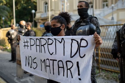 Una mujer sostiene una pancarta que dice "Dejen de matarnos" frente a una línea de policías antidisturbios durante una protesta convocada por activistas contra el asesinato de personas negras durante las operaciones policiales en favelas