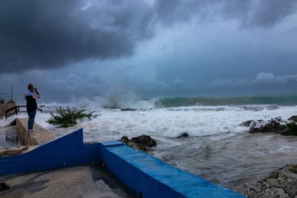 Una mujer toma fotos mientras las olas chocan contra un malecón mientras el huracán Ian pasa por George Town, isla de Gran Caimán, el lunes 26 de septiembre de 2022.