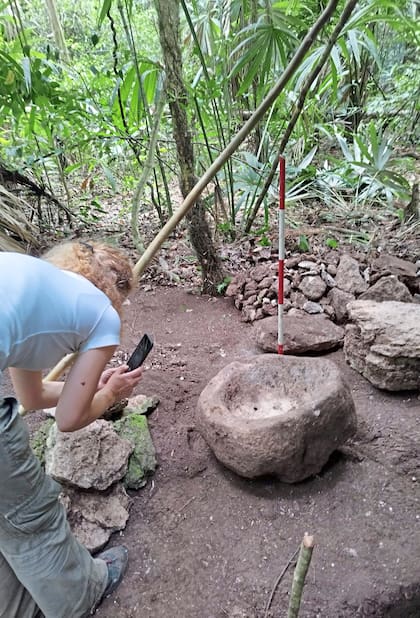 Una mujer tomando fotografías a una pieza descubierta en el yacimiento arqueológico de Uaxactún