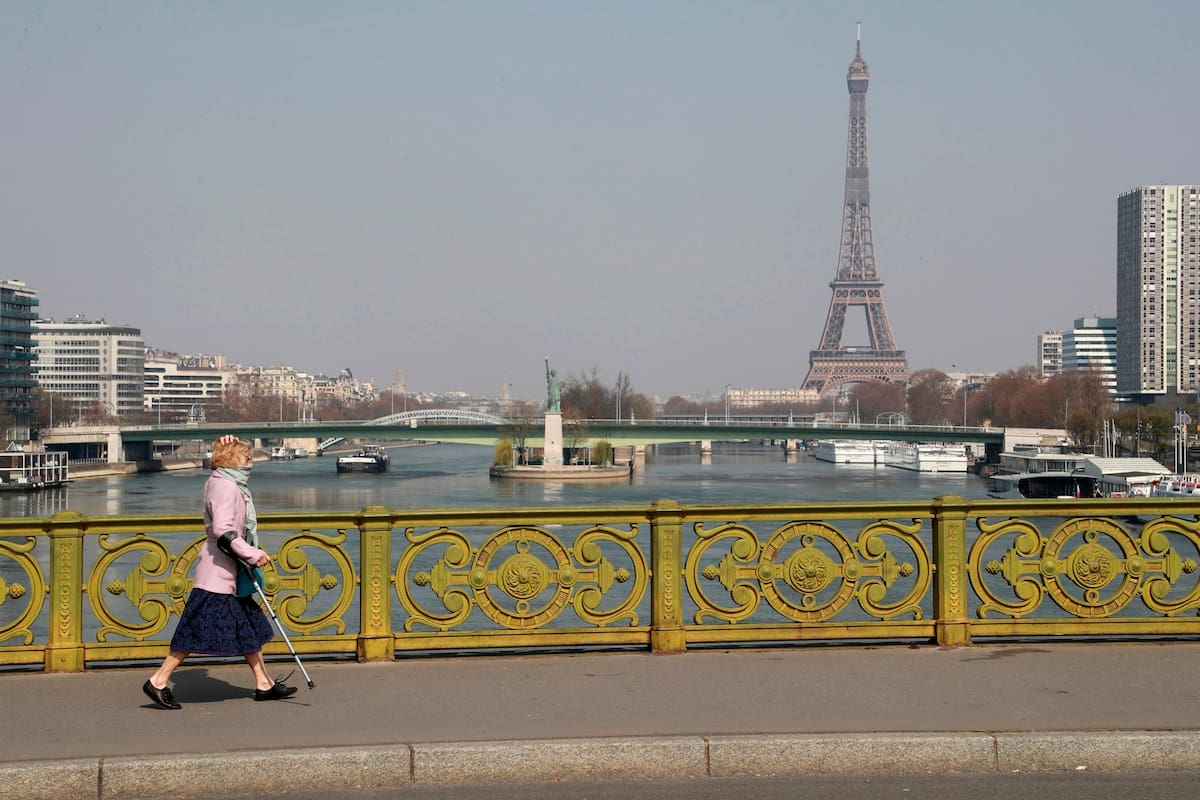 Una mujer usa su bufanda como protección protectora mientras camina por un puente frente a la Torre Eiffel el 28 de marzo de 2020, en París, en el duodécimo día de un encierro destinado a frenar la propagación de COVID-19