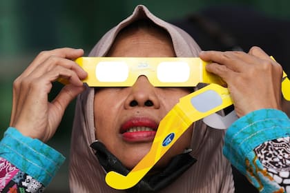 Una mujer utiliza gafas protectoras para ver un eclipse solar en Yakarta, Indonesia, el jueves 20 de abril de 2023. Los pocos afortunados en su ruta o bien vieron la oscuridad de un eclipse total o el “anillo de fuego” cuando el sol asomaba tras la Luna. (AP Foto/Tatan Syuflana)