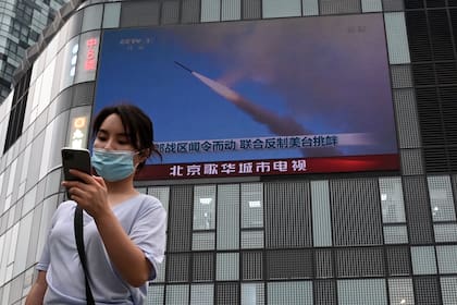 Una mujer utiliza su teléfono móvil mientras camina frente a una pantalla grande que muestra un noticiero sobre los ejercicios militares de China que rodean a Taiwán, en Pekín el 4 de agosto de 2022.