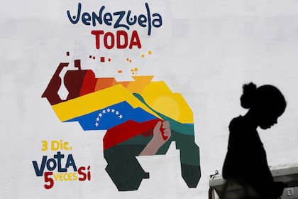 Una mujer vende frutas en Caracas junto a un mural con el mapa de Venezuela incorporando la región guyanesa de Esequibo