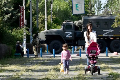 Una mujer y un niño caminan por un parque mientras los militares rusos patrullan la calle en Skadovsk, óblast de Kherson