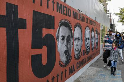 Una niña señala un mural con el rostro del presidente brasileño Jair Bolsonaro durante una protesta por su manejo de la pandemia del COVID-19 en la avenida Paulista, en Sao Paulo, Brasil, el sábado 19 de junio de 2021. (AP Foto/Marcelo Chello)