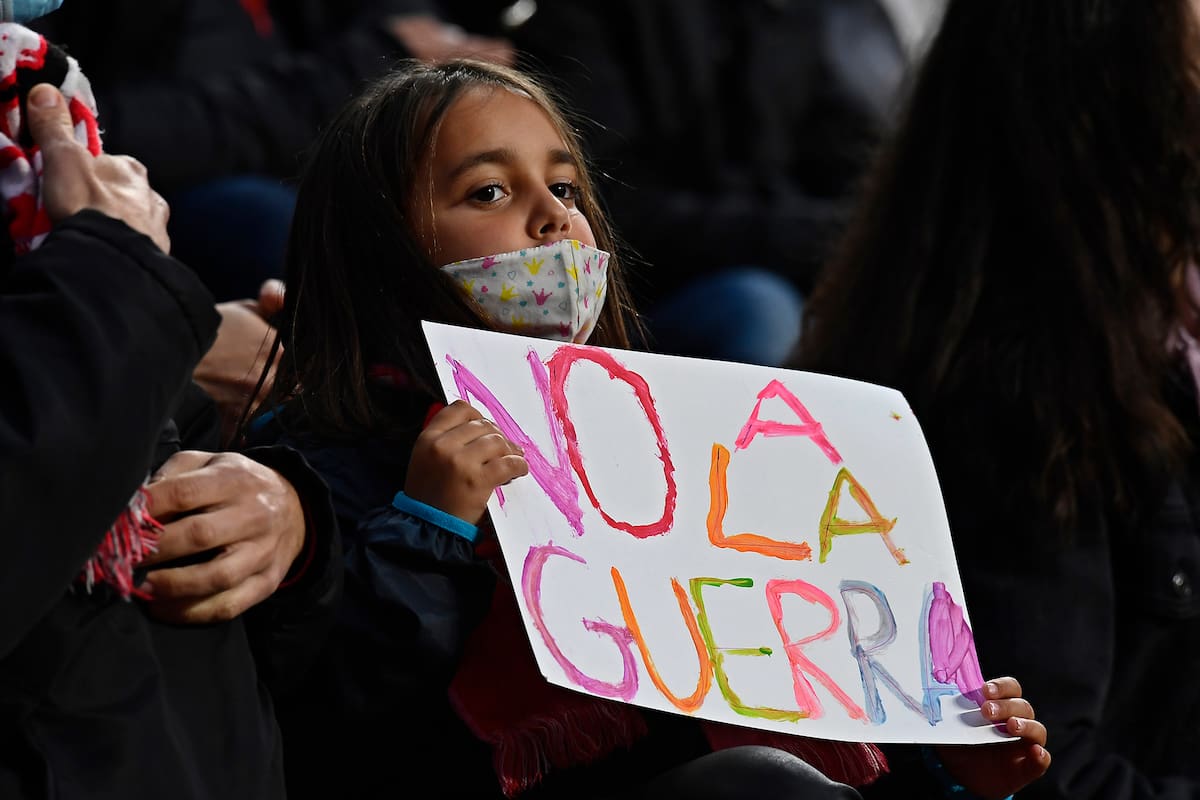 Una niña sostiene un mensaje que dice "No a la guerra" en las gradas antes del inicio de un partido