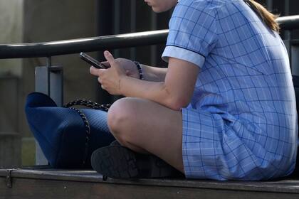 Una niña utiliza un celular sentada en un banco en Sydney, Australia