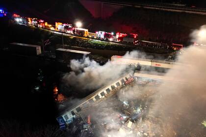 Una nube de humo emerge de vagones de tren mientras bomberos y rescatistas trabajan luego de un choque de trenes cerca de la ciudad de Larissa, Grecia, el miércoles 1 de marzo de 2023. (AP Foto/Vaggelis Kousioras)