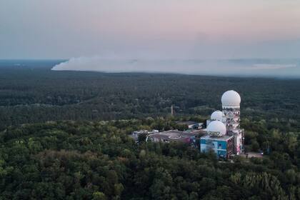 Una nube de humo se eleva sobre el bosque Grunewald, por detrás del antiguo radar de la Agencia Nacional de Seguridad, en lo alto de la Teufelsberg, en Berlín, Alemania, el 4 de agosto de 2022. (AP Foto/Michael Sohn)