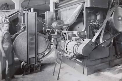 Una operaria de pie junto a una máquina para cardar llamada Silver Roll Former