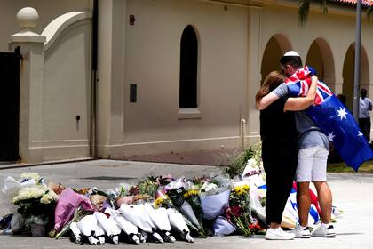 Una pareja coloca flores como homenaje a las víctima de un tiroteo ante el Bondi Pavilion en el distrito de Bondi Beach, Sydney, el lunes 15 de diciembre de 2025, al día siguiente de la balacera. (AP Foto/Mark Baker)
