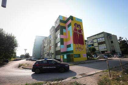 Una patrulla de la policía circula por el Parco Verde de Caivano, donde puede verse un mural de dos niñas que dice "Nadie se queda solo"