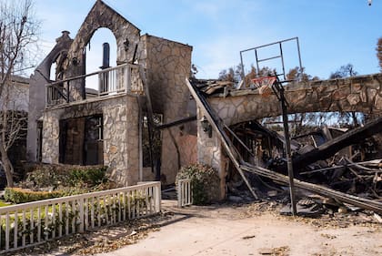 Una pelota de baloncesto se ve enganchada en la red delante de una casa destruida en el incendio de Palisades en el vecindario de Pacific Palisades en Los Ángeles, el viernes 24 de enero de 2025. (AP Foto/Damian Dovarganes)