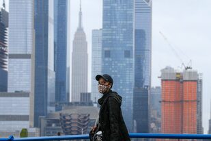 Una persona con una máscara facial camina en Weehawken, Nueva Jersey, el 11 de noviembre de 2020, con el horizonte de Nueva York de fondo, que sufre un aumento de casos de coronavirus