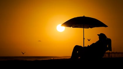 Una persona descansa bajo una sombrilla durante la puesta del sol en Newport Beach, California (Archivo)